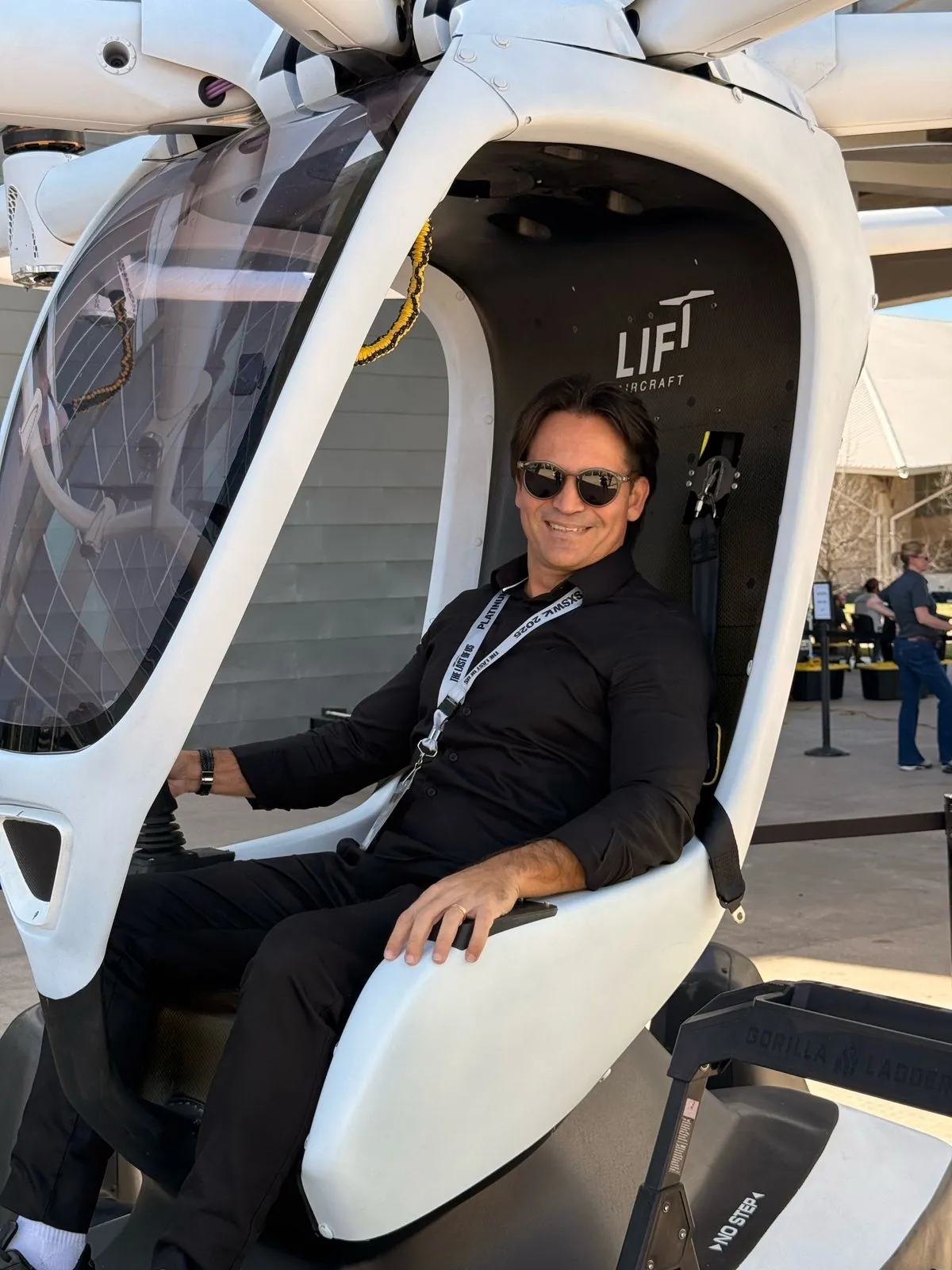 Ivaldo sorrindo, de óculos escuros e camisa preta, sentado na cabine branca do HEXA, com o logo da LIFT Aircraft atrás