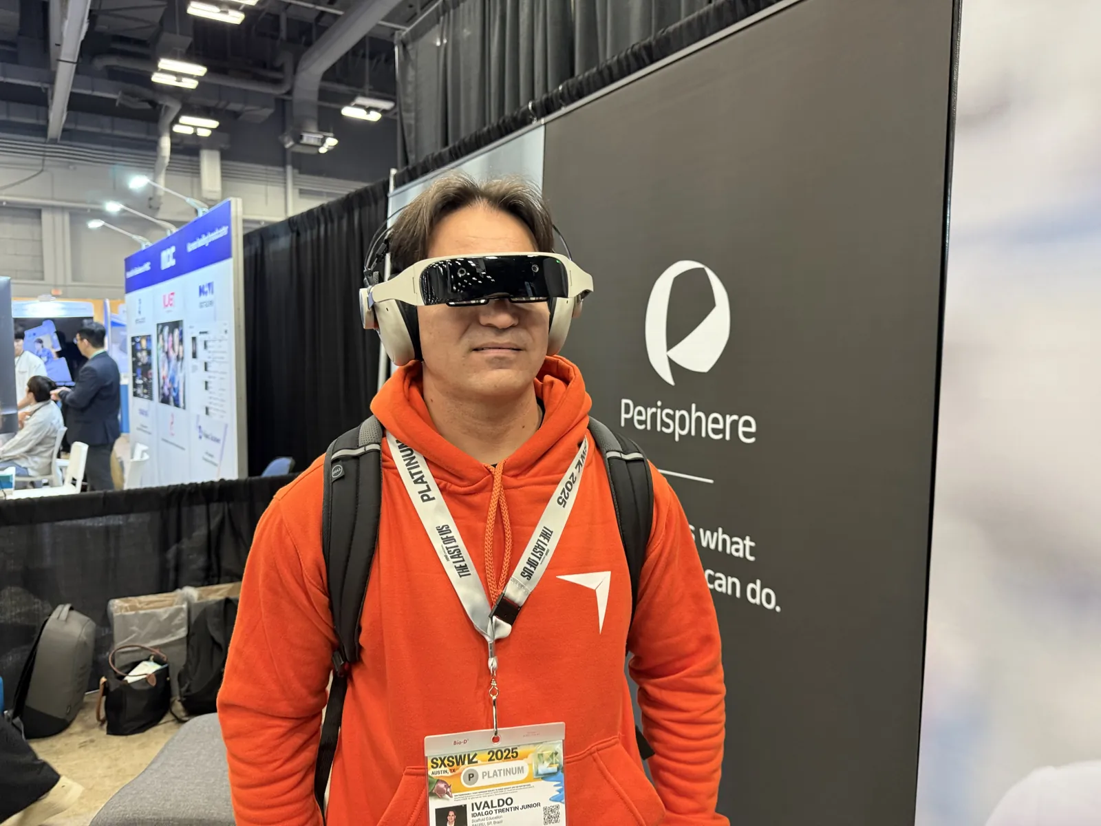 Ivaldo usando o Perisphere, um fone de ouvido branco com visor escuro sobre os olhos, ao lado do painel da marca